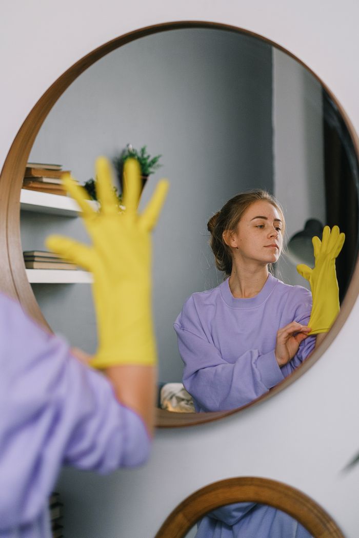 get-in-touch A woman wearing yellow gloves is reflected in a wall mirror indoors, exuding a serene expression.