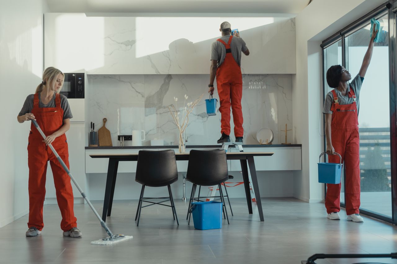 home-hero Group of cleaners in red uniforms mopping and wiping glass in a modern dining room.
